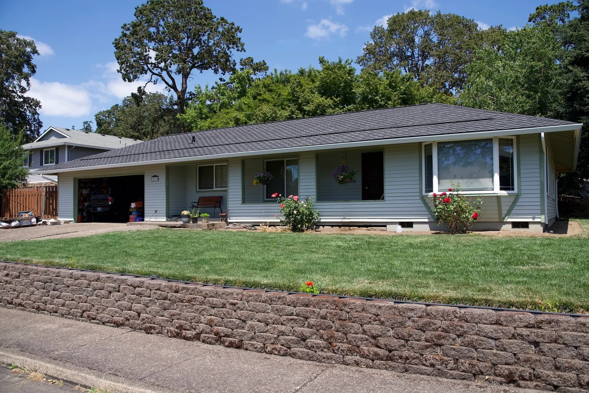 Street-level front elevation of a Gladstone, OR ranch house with light blue siding, white gutters, and a new dark gray shingle roof