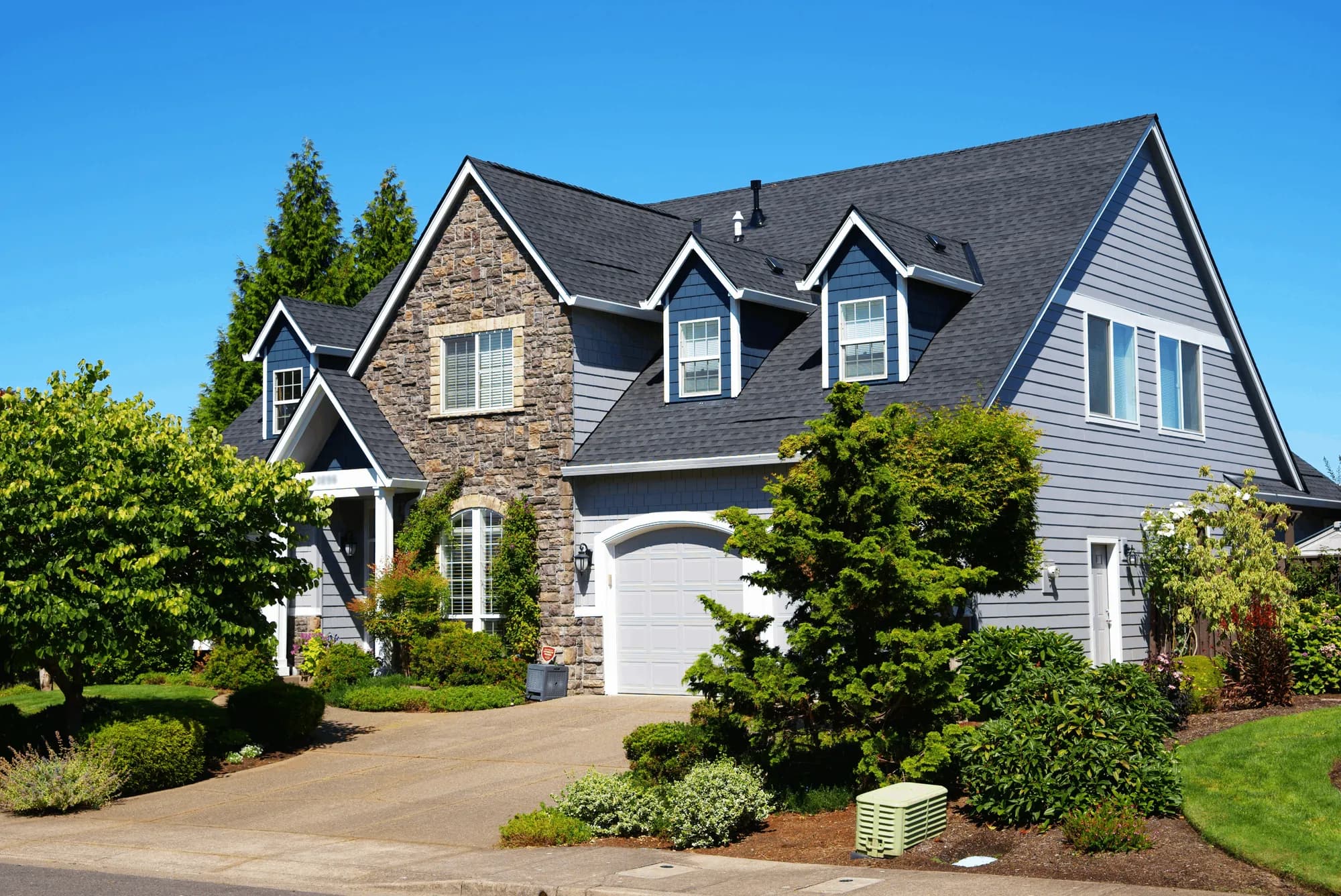 Street view of a two-story Salem, OR house with a completed charcoal shingle roof, stone entry gable, and dormers